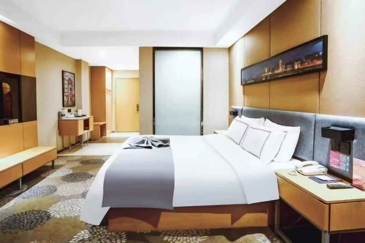A hotel room with a bed, bedside table, and a desk with a chair.