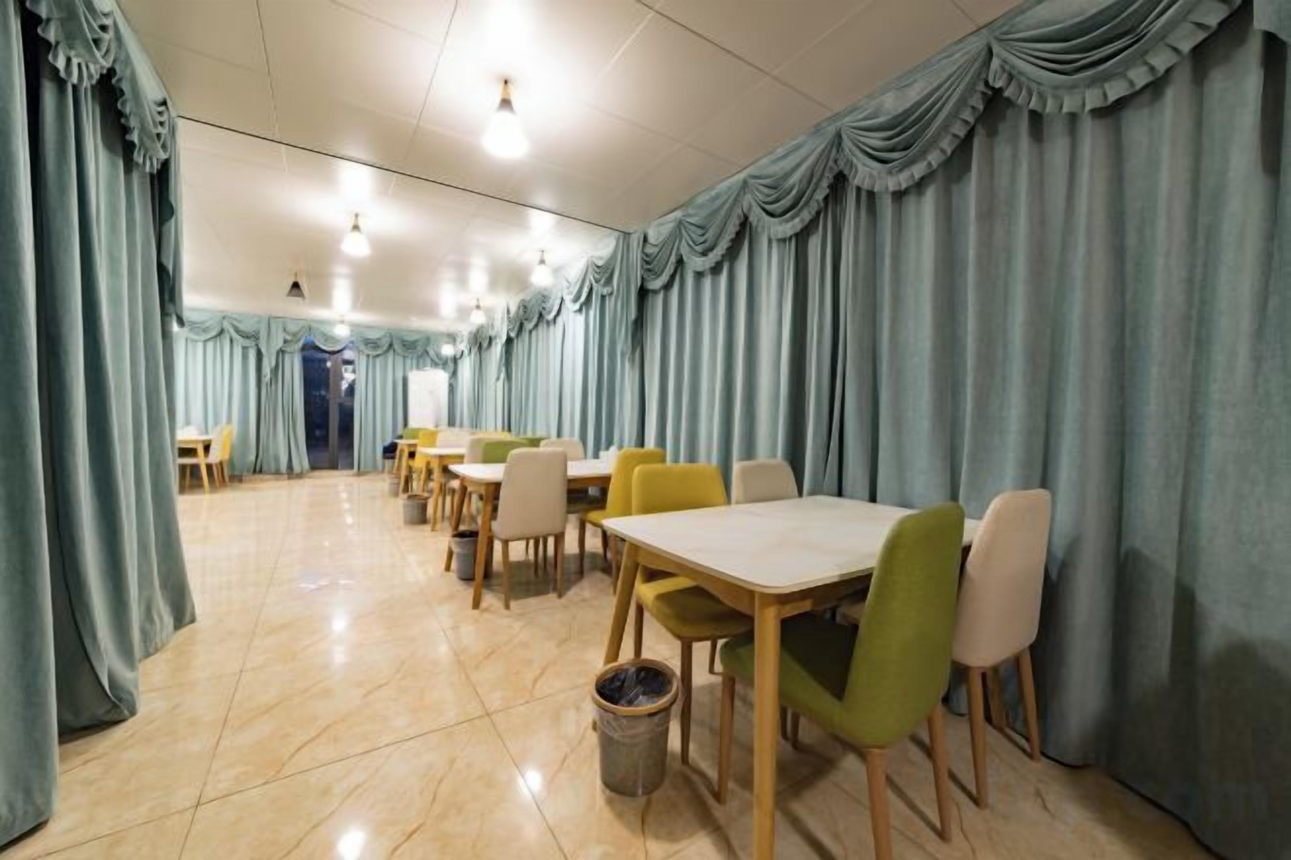 A dining area with tables and chairs, a trash bin, and curtains.