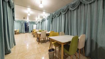 A dining area with tables and chairs, a trash bin, and curtains.