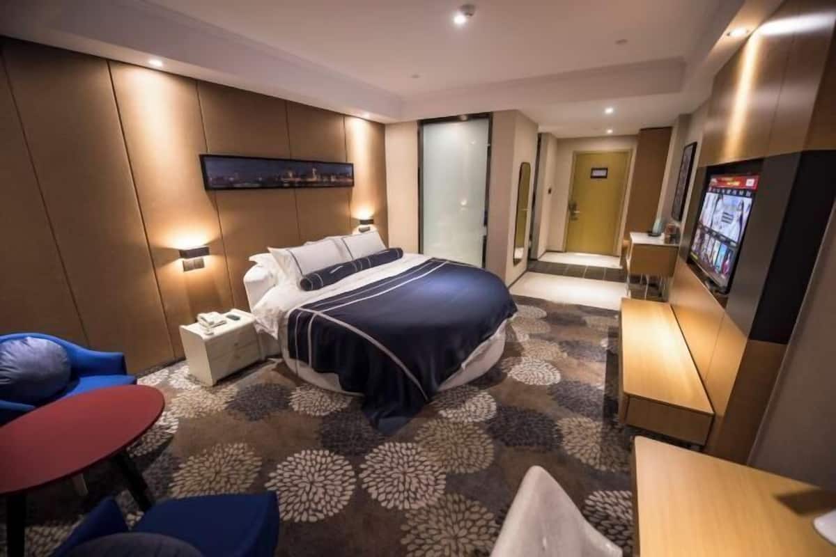 A hotel room with a bed, bedside tables, a TV, a seating area with a table, and a carpeted floor.