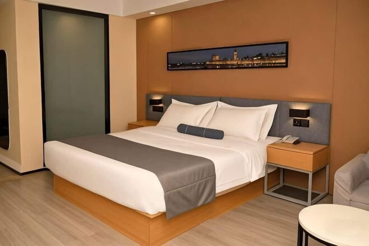 A modern hotel room with a large bed, bedside tables, a chair, and a cityscape view.