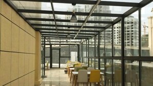Un espace de restauration intérieur moderne, doté de murs en verre, d’un sol carrelé et d’une rangée de tables et de chaises.
