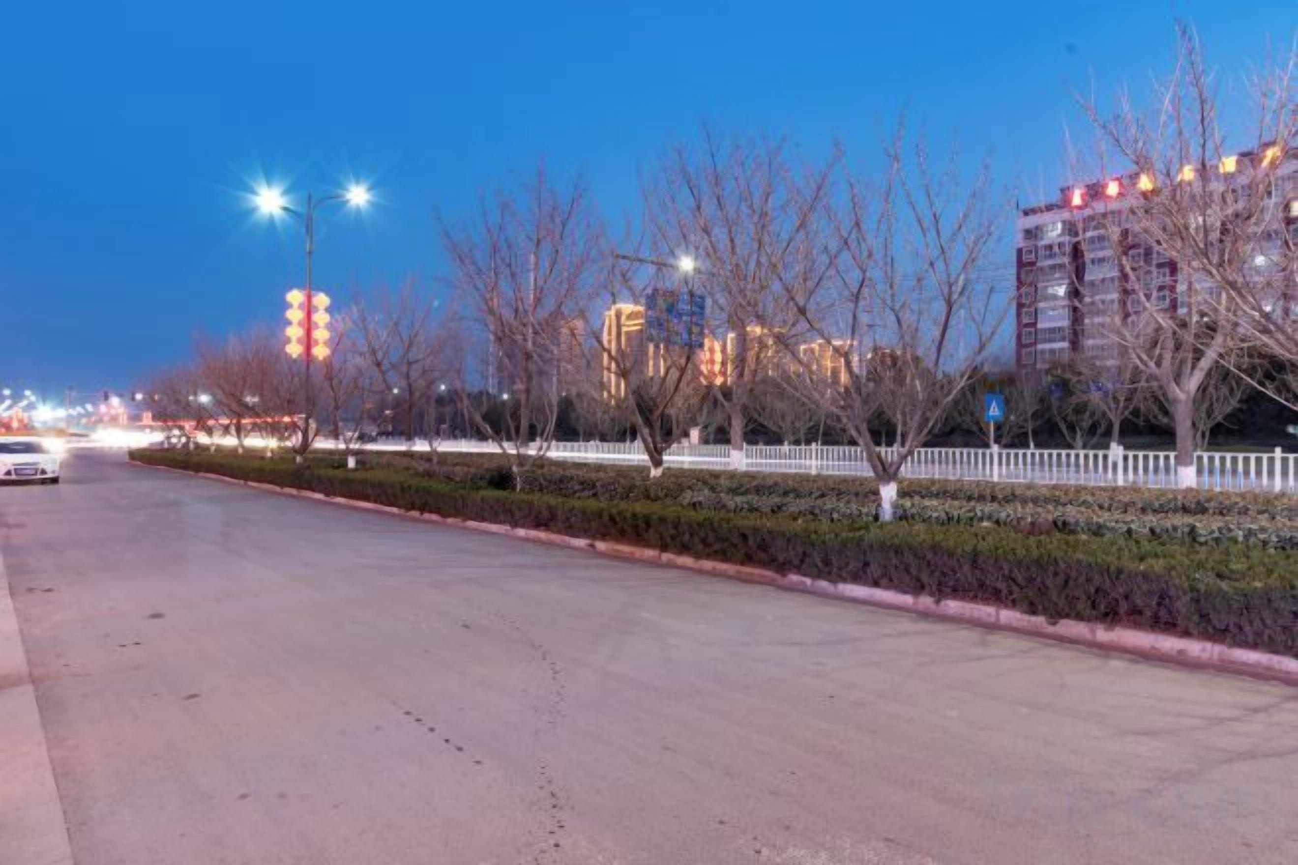 A wide street with a sidewalk, trees, and buildings in the background.