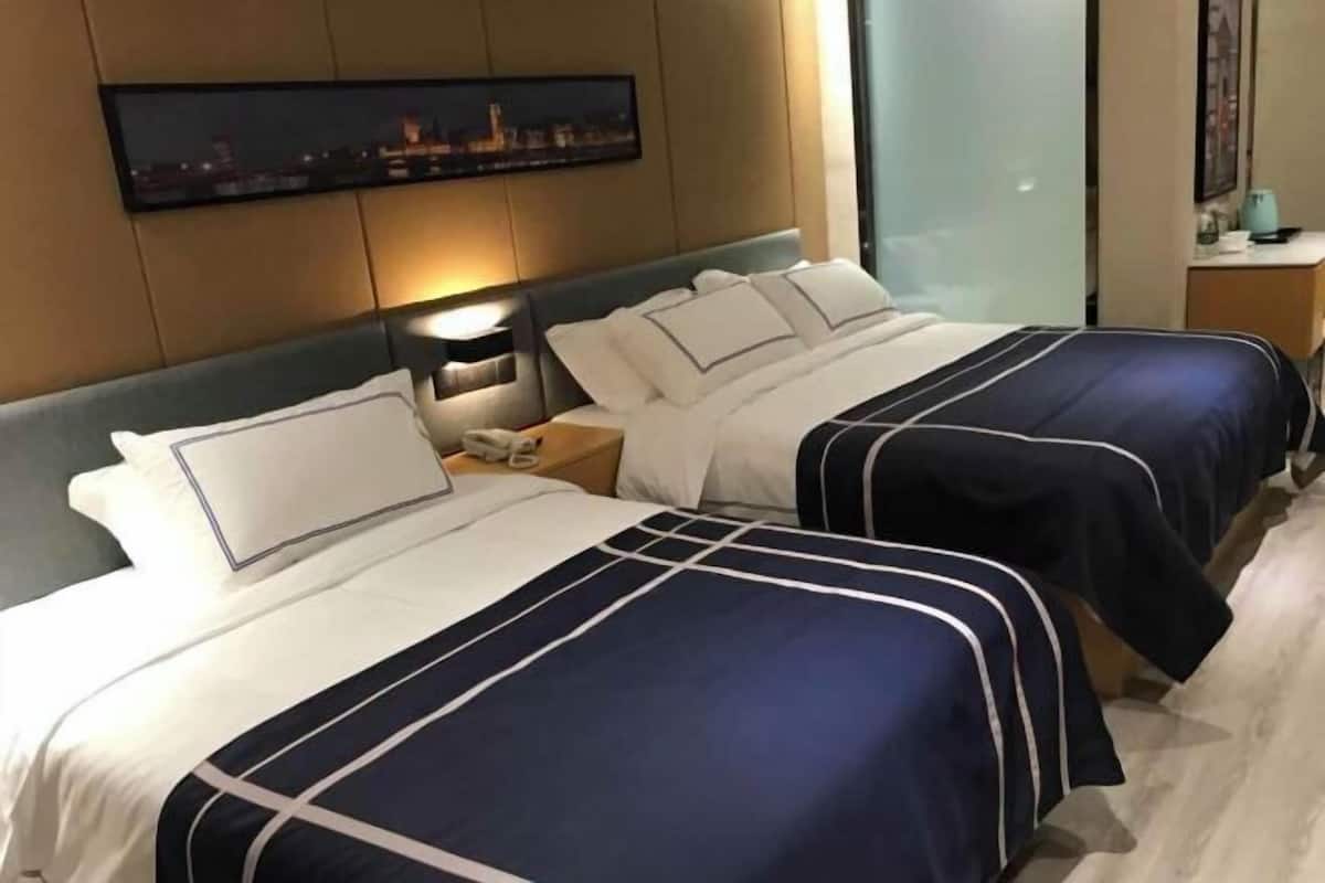 A hotel room with two beds, a nightstand, a wall-mounted TV, and a cityscape view.