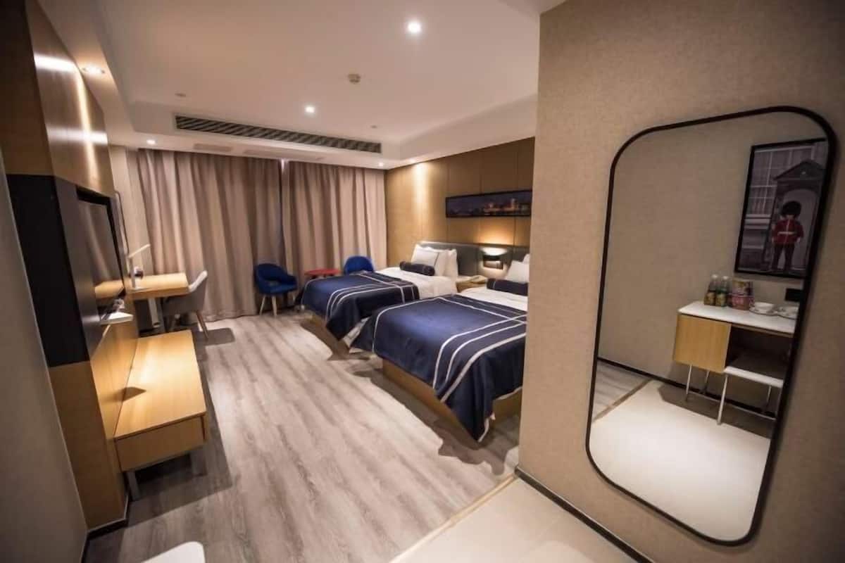 A hotel room with two beds, a desk, a chair, a mirror, and a small kitchenette.