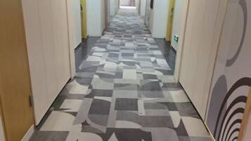 A hotel corridor with patterned carpet, doors on both sides, and emergency exit signs.