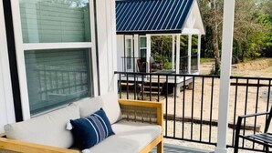 Une terrasse en bois avec un canapé et une petite table, un espace extérieur couvert avec un toit bleu, et un bâtiment blanc doté de grandes fenêtres.