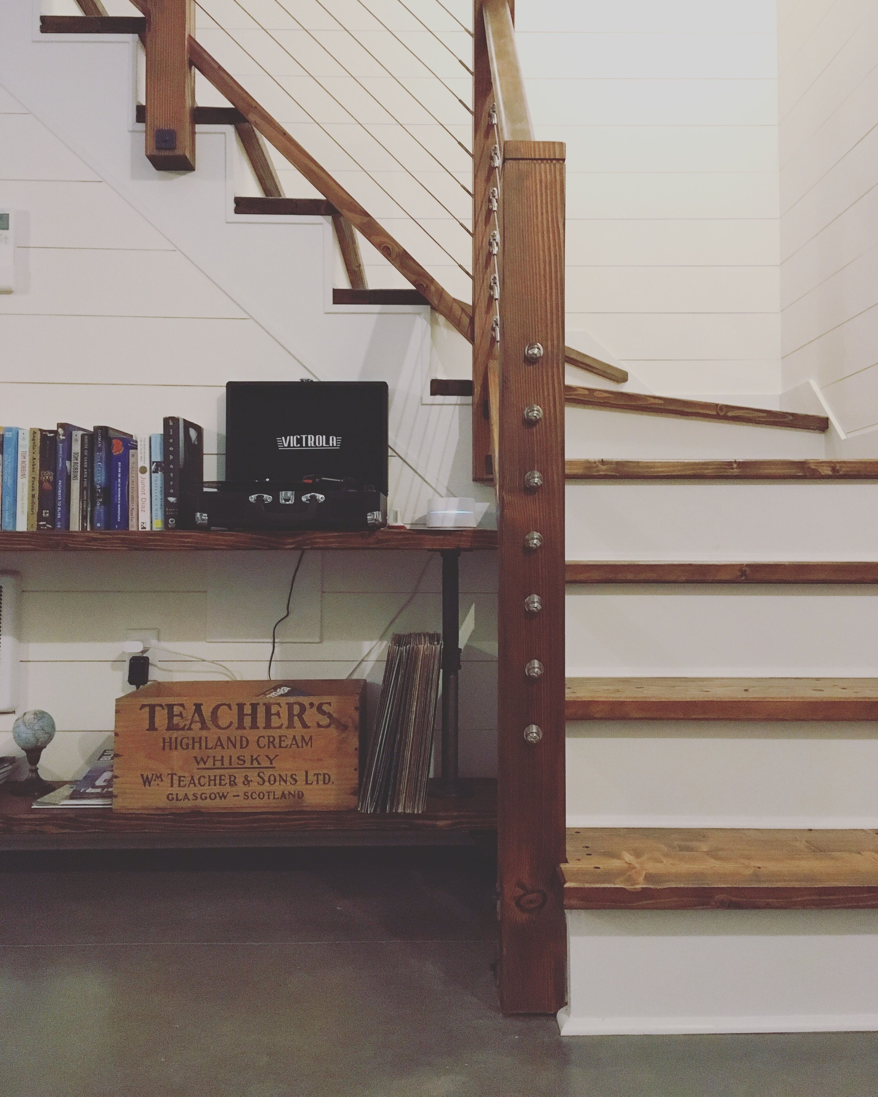 Una escalera con barandas de madera y un estante con libros y un dispositivo electrónico negro.