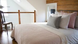 Een slaapkamer met een groot bed, een houten hoofdbord, een raam met zonwering en een stoel.
