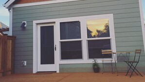 Een gelijkvloers huis met een groene gevelbekleding, een witte voordeur en een grote schuifpui. Er is een klein terras met een houten tafel en twee stoelen.