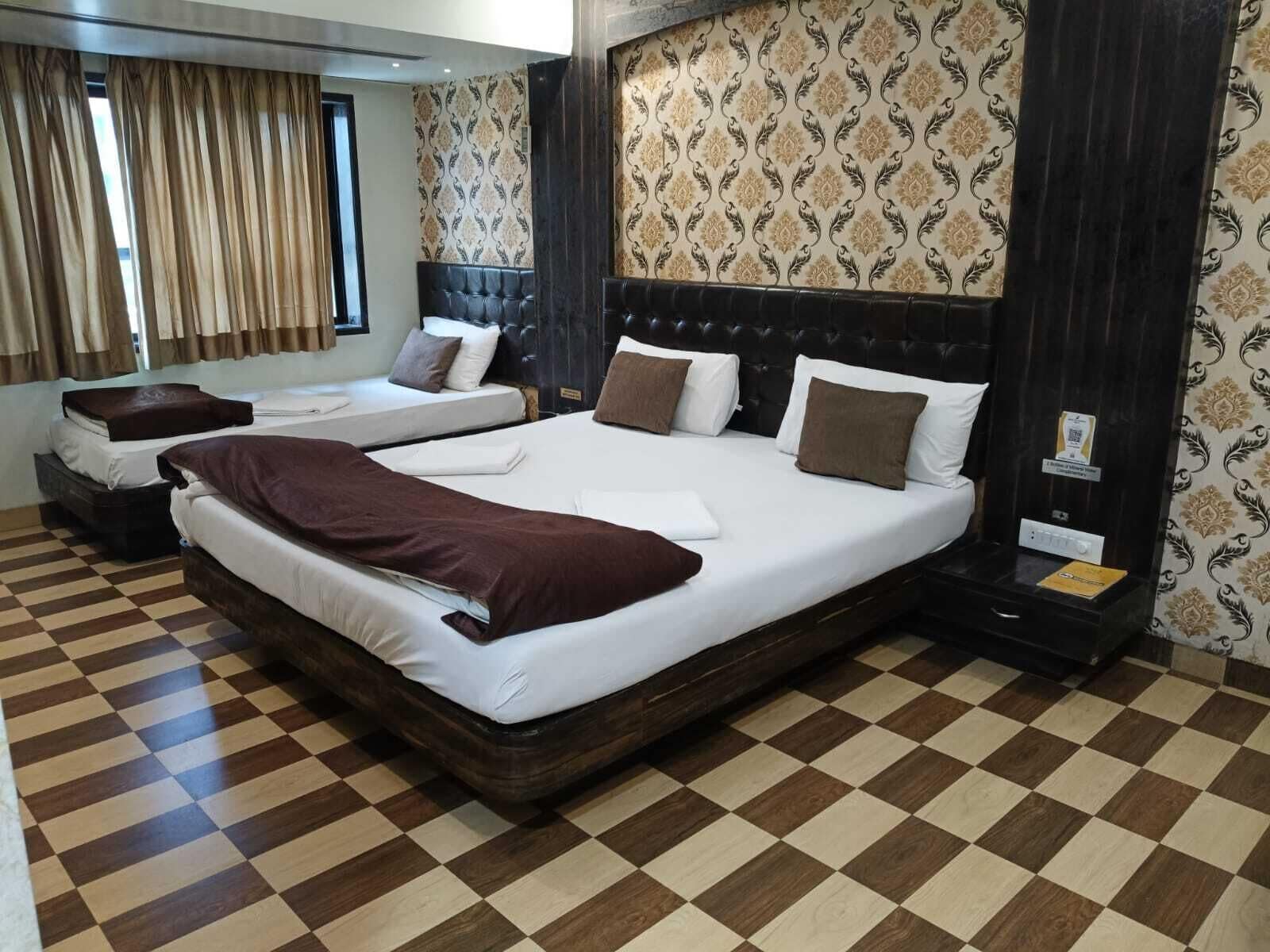 Une chambre d’hôtel avec deux lits, un sol à carreaux, un papier peint à motifs et une tête de lit sombre.