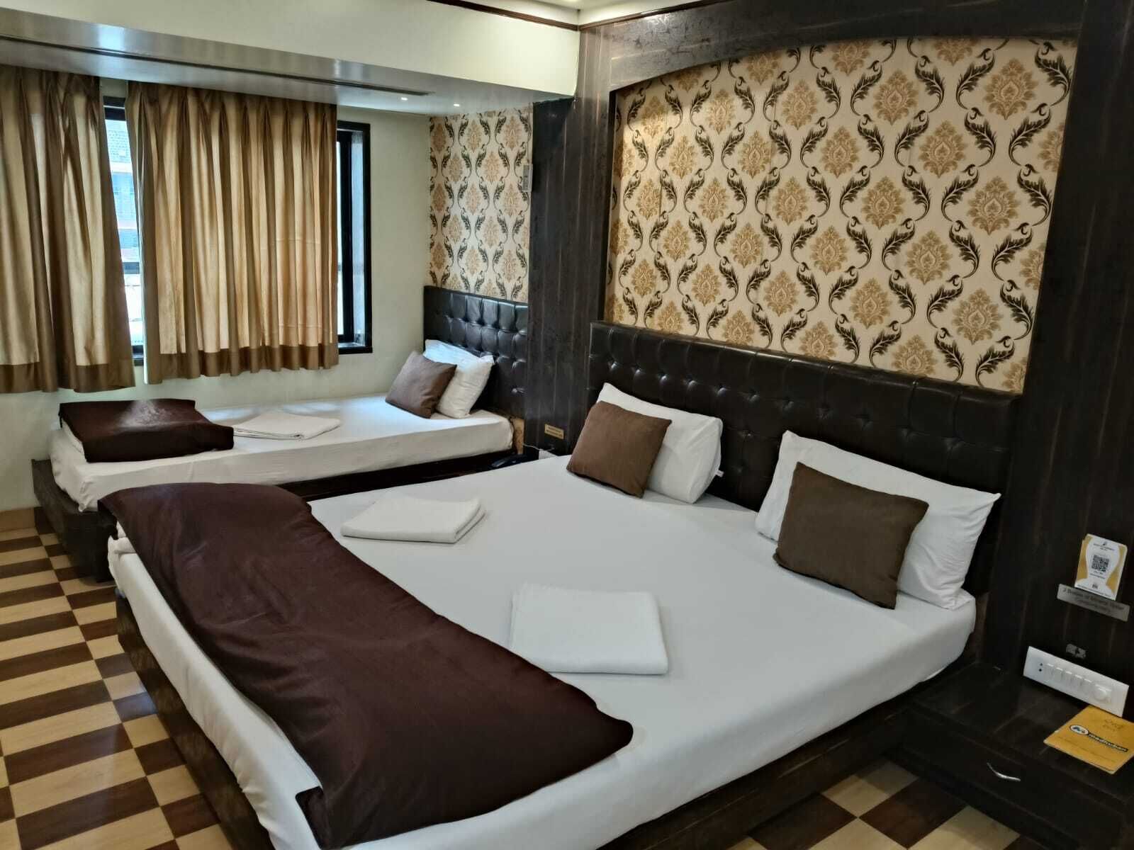 A hotel room with two beds, checkered floor, patterned wallpaper, and a window with curtains.