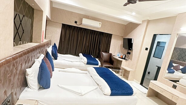 A hotel room with a large bed, a desk, a chair, an air conditioning unit, and a ceiling fan. - Saibaba International Hotel (Rahata)