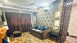A modern living room with a sectional sofa, a bright orange armchair, and a patterned wall. - Saibaba International Hotel (Rahata)