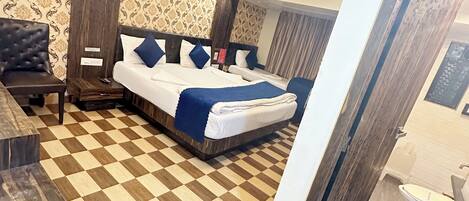 Habitación de hotel con suelo a cuadros, una cama con ropa de cama azul, un sillón de cuero oscuro y una mesita de noche de madera.