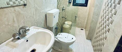 Un baño pequeño con lavamanos, inodoro y bidé. Las paredes están cubiertas de azulejos con un diseño a cuadros.