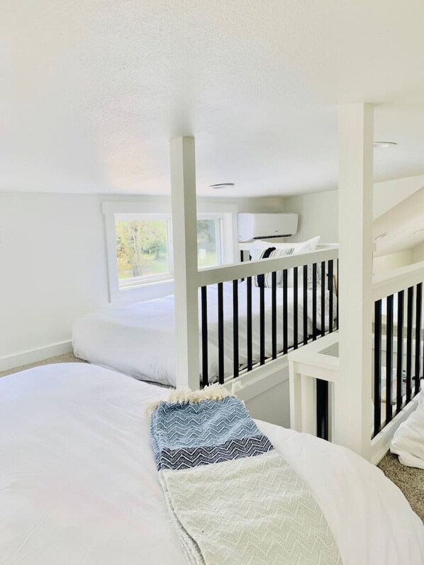 A bedroom with a bunk bed, a window with a view of trees, and a white ceiling. - Arrow Acres Tiny Home - June (Warren)