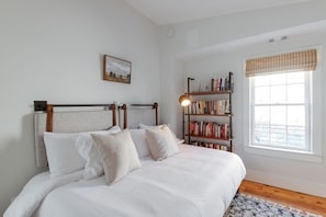 Een slaapkamer met een bed, een boekenkast, een raam met uitzicht en een schilderij aan de wand.