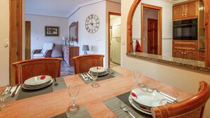 A dining area with a wooden table set for four, a clock on the wall, and wooden cabinets in the background.