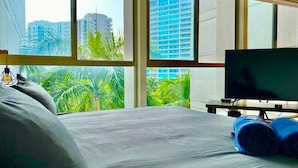 A hotel room with a bed, a television, and a window with a view of palm trees and buildings. - Relax in front of Ixtapa's beautiful Marina. (Ixtapa Zihuatanejo)
