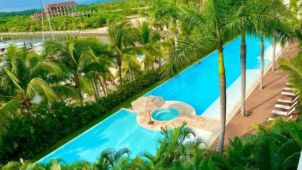 A large swimming pool with a hot tub, surrounded by palm trees and a view of a mountain range. - Relax in front of Ixtapa's beautiful Marina. (Ixtapa Zihuatanejo)