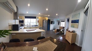 Uma cozinha moderna com uma ilha central, uma sala de jantar com mesa e cadeiras de madeira, e um espaço de estar com sofá e televisão.