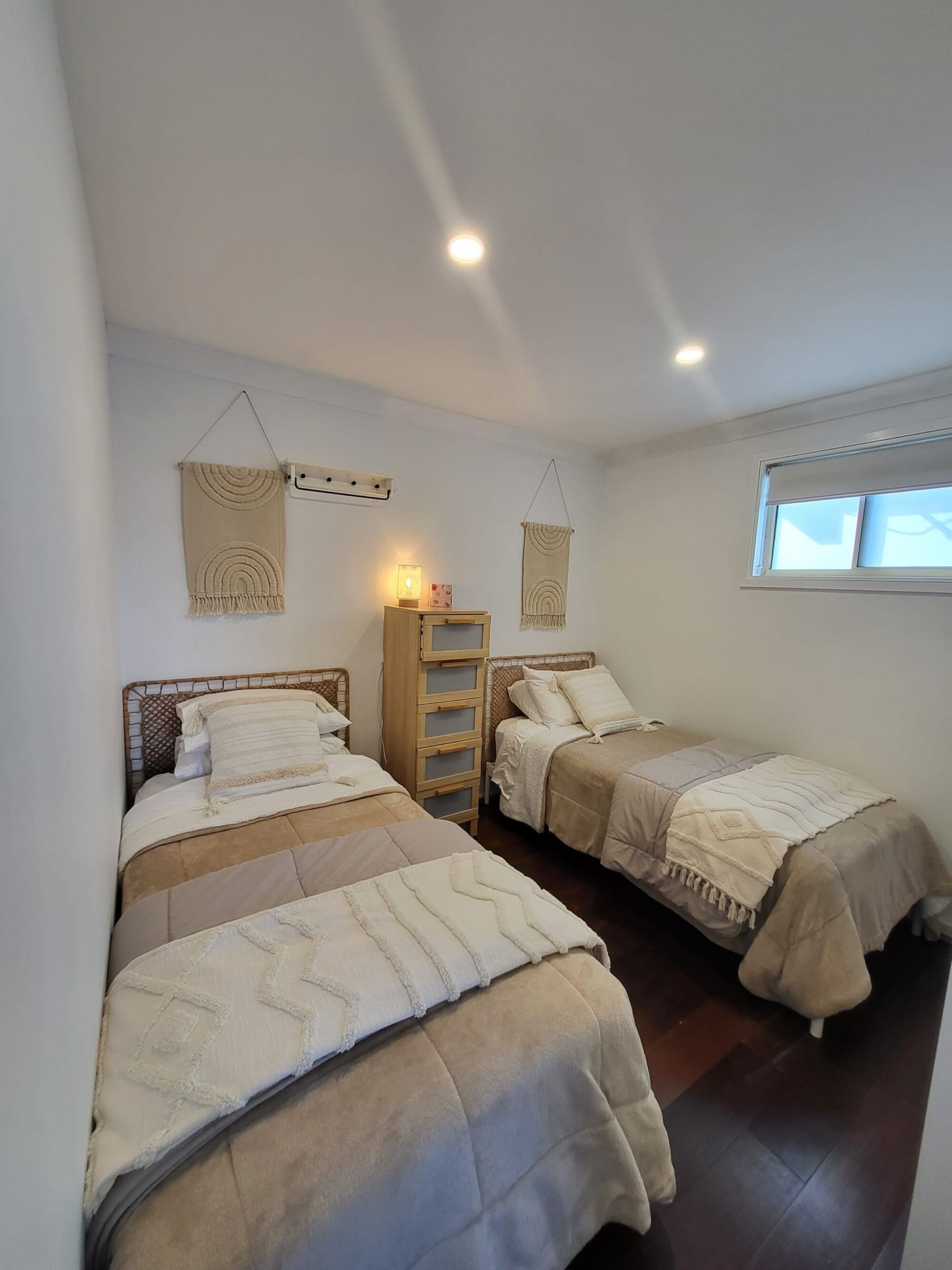 A room with three beds, a wooden nightstand, and wall-mounted macramé hangings.