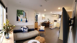 Uma sala de estar moderna com um sofá, uma mesa de centro redonda e uma área de jantar com mesa e cadeiras.