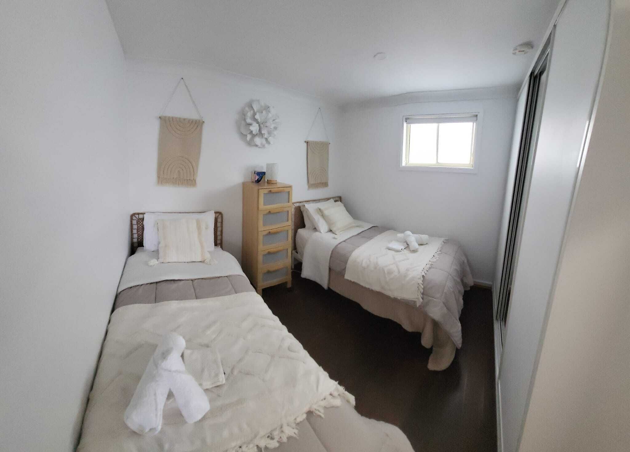 Una habitación pequeña y limpia con dos camas, un aparador de madera y una ventana.