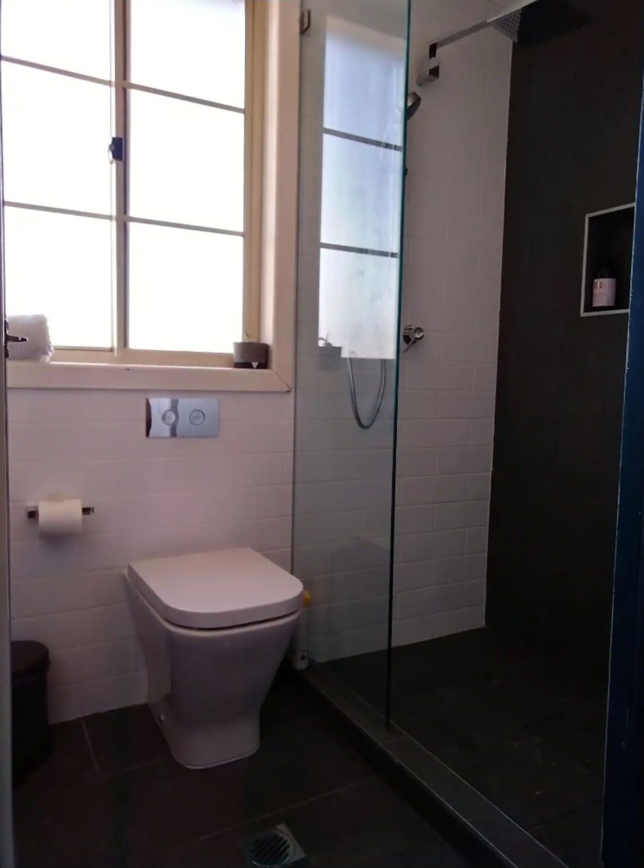 Une salle de bain moderne avec des toilettes, une douche à parois de verre et une fenêtre.