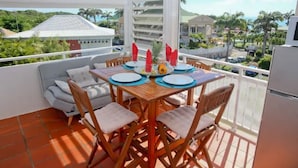 Varanda com mesa posta para quatro pessoas, cadeiras e uma geladeira.