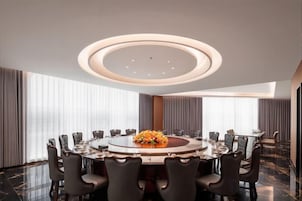 Un salón de conferencias con una mesa redonda, sillas y un arreglo floral central.