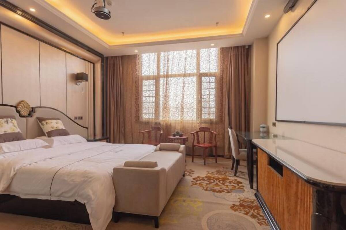A hotel room with a large bed, a desk, and a large window with curtains.