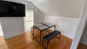 A small, open room with a wooden floor, a black table with a bench, and a TV mounted on the wall.