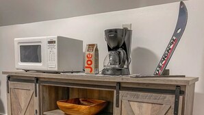 A wooden cabinet with a microwave, coffee maker, and a bag of coffee on top.