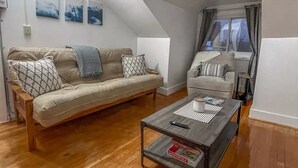 A cozy living room with a wooden floor, a sofa, a coffee table, and a window with curtains.