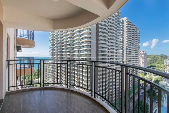 A balcony with a curved railing overlooking a high-rise building and a body of water.