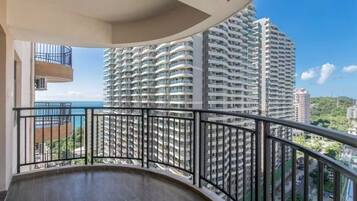 A balcony with a curved railing overlooking a high-rise building and a body of water.