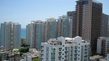 Un edificio residencial de gran altura con múltiples balcones, cielo despejado y vista al mar.