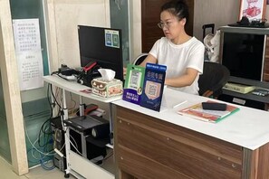 Un comptoir d’accueil avec un ordinateur, un téléphone et une tasse de café. On y trouve également quelques livres et un code QR.