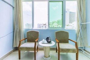 Une pièce avec deux chaises, une petite table et une fenêtre donnant sur des immeubles.
