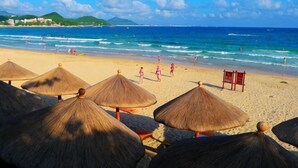 Ein Strand mit reetgedeckten Sonnenschirmen, sandigem Ufer und dem Meer.