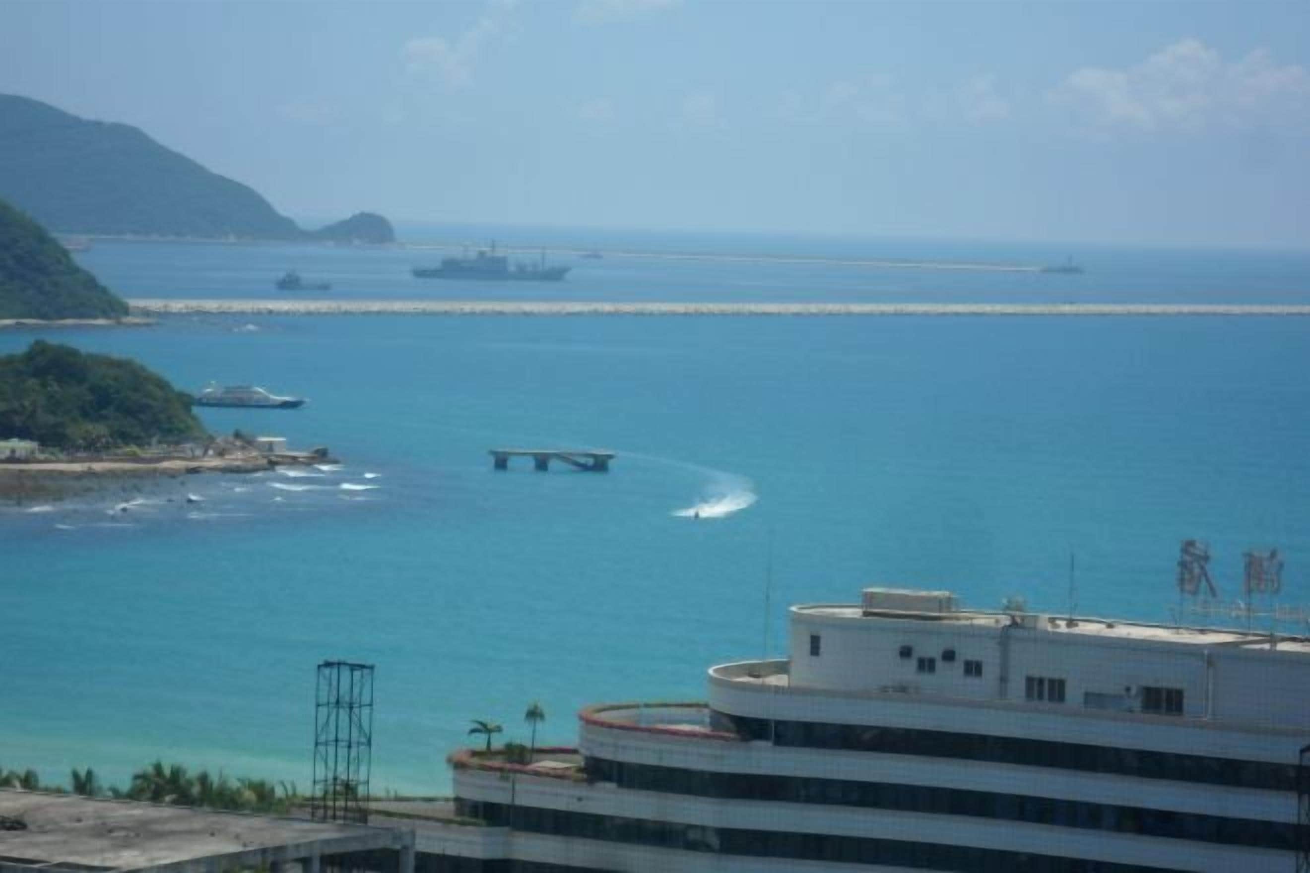 Vista costera con un puente, mar tranquilo y barcos a la distancia.