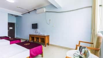 A hotel room with two beds, a television, a table with a kettle, and a chair.