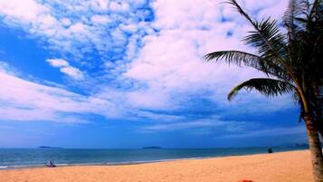 A beach with a person lying on the sand, palm trees, and a clear sky.