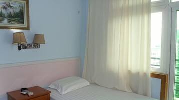 A hotel room with a bed, a nightstand, two wall-mounted lamps, a painting, and a window with curtains.
