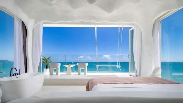 Ein modernes Schlafzimmer mit einem großen Bett, einer Badewanne und einem Balkon mit Blick auf das Meer.