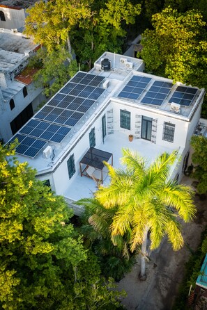 A building with solar panels on the roof, surrounded by lush greenery and trees.