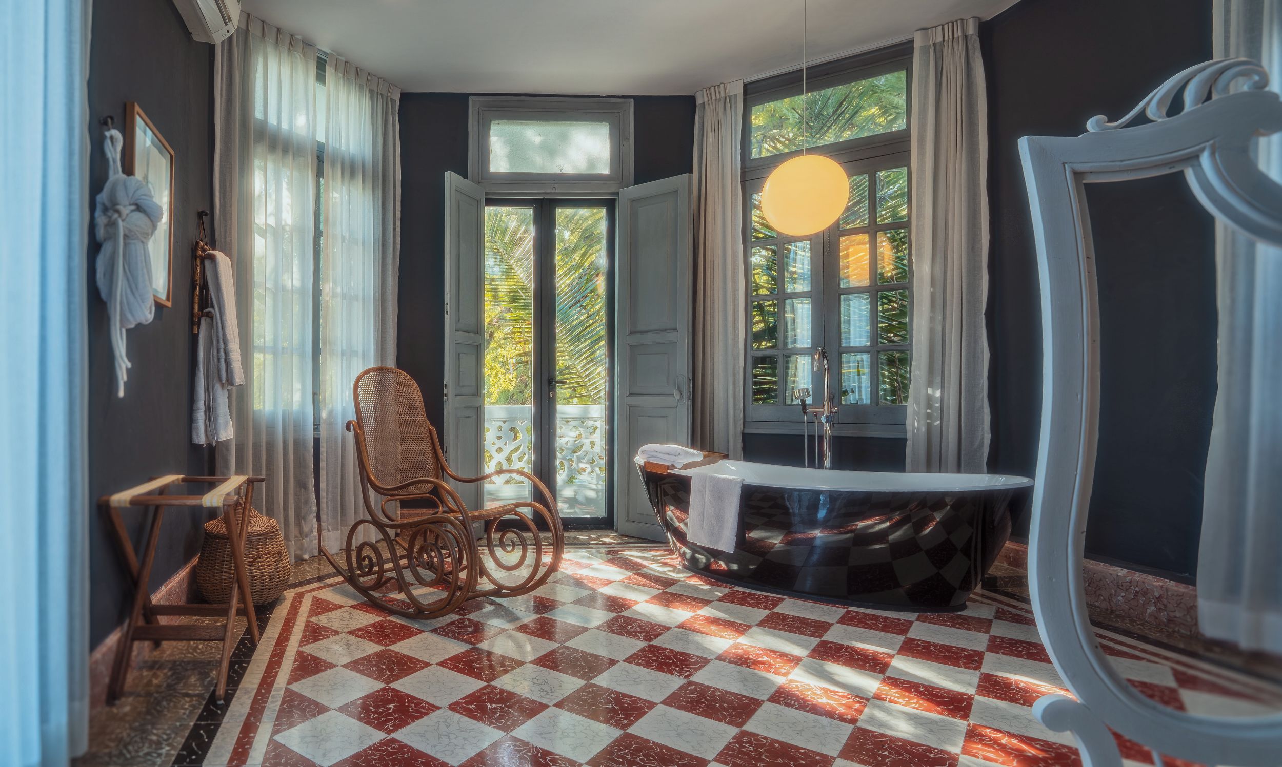A bathroom with a checkered floor, a bathtub, a wicker chair, and a large mirror.