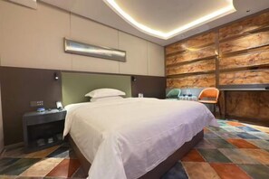 A modern hotel room with a large bed, a nightstand, a chair, and a wall-mounted shelf.